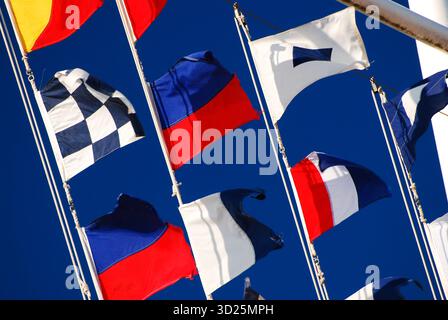 Bandiere nautiche colorate che rappresentano l'onda dell'alfabeto nella brezza di una barca vicino a un porticciolo Foto Stock