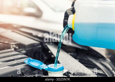 Dettaglio primo piano della mano del conducente o meccanico nei guanti che versano liquido antigelo blu per lavaggio parabrezza invernale auto con annaffiatoio bootle Foto Stock