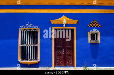 Xalapa, stato di Veracruz, Messico. Tipica facciata colorata in blu e giallo con porte in legno intagliato e finestre ornate a sbarre. Foto Stock