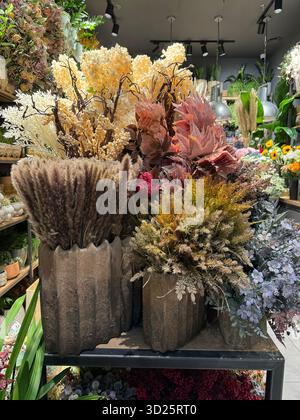 Un'esposizione riccamente strutturata di composizioni di fiori artificiali e secchi assortite in un ambiente di vendita al dettaglio, con sfumature di marrone, beige, rosa e giallo Foto Stock