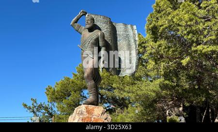 Eroica statua in bronzo di Spyros Kayales che innalza la bandiera greca al parco Venizelos Graves di Akrotiri, Chania, Creta, Grecia, con sfondo marino. Foto Stock