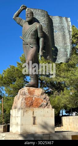 Eroica statua in bronzo di Spyros Kayales che innalza la bandiera greca al parco Venizelos Graves di Akrotiri, Chania, Creta, Grecia, con sfondo marino. Foto Stock