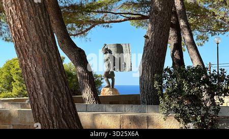 Eroica statua in bronzo di Spyros Kayales che innalza la bandiera greca al parco Venizelos Graves di Akrotiri, Chania, Creta, Grecia, con sfondo marino. Foto Stock