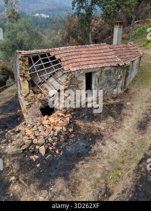 Vista aerea di una vecchia casa in pietra parzialmente crollata con un tetto piastrellato rosso circondato da terra bruciata dopo un incendio Foto Stock