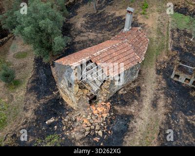 Vista aerea di una vecchia casa in pietra parzialmente crollata con un tetto piastrellato rosso circondato da terra bruciata dopo un incendio Foto Stock