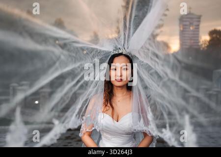 Sposa cinese con abito da sposa e velo accanto alla fontana Foto Stock