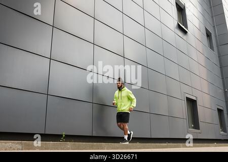 Un atletico afroamericano si allena facendo jogging all'aperto, vestito con una felpa verde con cappuccio. Foto Stock