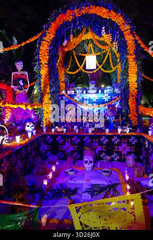 Altare colorato illuminato il giorno dei morti decorato con fiori di calendula, candele, scheletri e offerte tradizionali di notte Foto Stock