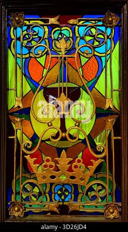 Vetrata colorata con dettagli decorati in ferro battuto dorato e motivi geometrici e floreali simmetrici Foto Stock