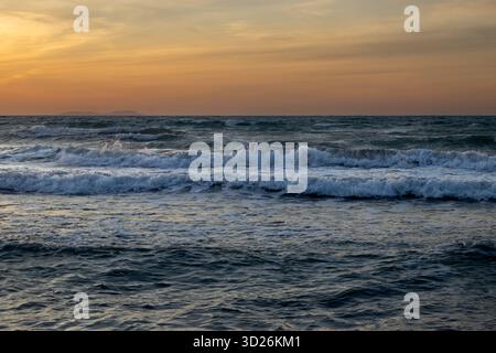 Mare dello Ionio con onde durante una tarda giornata estiva. Isola Erikousa sullo sfondo. Cielo colorato al tramonto. A nord dell'isla Foto Stock