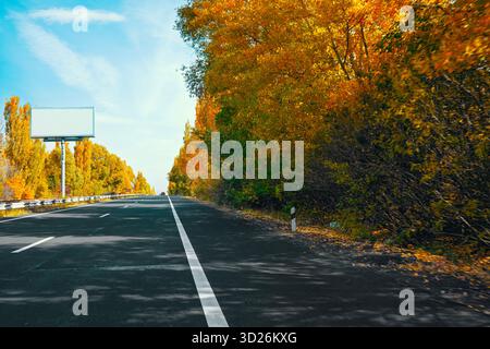 Una strada con un cartellone sullo sfondo e alberi sul lato. La strada è vuota e gli alberi sono pieni di foglie Foto Stock