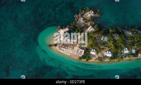 Una vista aerea di un'isolata isola tropicale o penisola, caratterizzata da edifici bianchi e vegetazione lussureggiante. Foto Stock