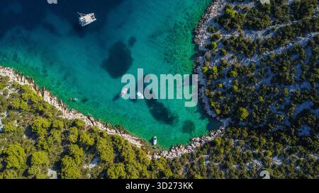 Vibrante contrasto di una costa rocciosa soleggiata e di un mare sereno e turchese punteggiato di barche da diporto. Foto Stock