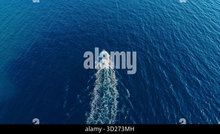 Potente imbarcazione che traccia un percorso di schiuma bianca attraverso il vasto e profondo mare blu, svela una firma fugace sulla superficie dell'acqua. Foto Stock