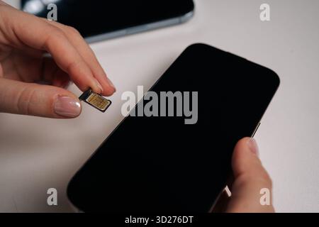 Mani femminili che tengono la scheda sim e il nuovo smartphone su un tavolo bianco, preparano l'inserimento della scheda sim e attivano il servizio mobile per un funzionamento senza problemi Foto Stock