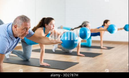 Classe di uomini e donne di diverse età in abbigliamento attivo che si allenano con mini palle durante l'allenamento Pilates insieme nel centro di riabilitazione Foto Stock