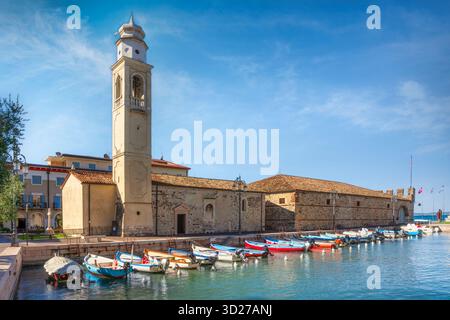 Vista sul porticciolo di Lazise con la chiesa romanica, il campanile e le barche colorate attraccate nel porto sul Lago di Garda, regione Veneto, Italia Foto Stock