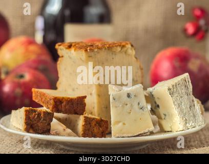La selezione di formaggi gourmet include il blu dana, gorgonzola e pepe Jack con vino e mele in un ambiente rustico Foto Stock