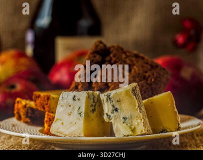 Gorgonzola al formaggio azzurro italiano e Jack al pepe sul piatto, brandy nero o bottiglia di vino e mele rosse dietro, atmosfera buia e accogliente Foto Stock