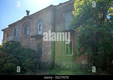 Erevan, Armenia 10.16.2025.Un grande edificio vecchio con un balcone e un albero davanti ad esso. L'edificio sembra essere stato abbandonato e necessita di essere riparato Foto Stock
