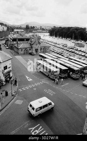 Caernarfon, Galles, una storica città fortificata, offre un'affascinante miscela di architettura medievale e moderni servizi costieri. Questa fotografia cattura una scena di strada trafficata vicino al castello di Caernarfon, mostrando il fulcro dei trasporti della città e la vicinanza allo stretto di Menai. L'immagine evidenzia il collegamento della città con il mare e il suo ruolo di punto di transito vitale all'interno del pittoresco paesaggio gallese. Foto Stock