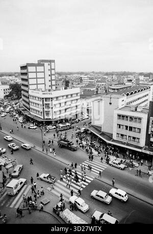 Le vivaci strade di Nairobi animano di vita in questa iconica fotografia degli anni '1960. L'iconico edificio KENVA domina lo skyline, una testimonianza del patrimonio architettonico della città. L'immagine cattura un'istantanea vibrante della vita quotidiana, con i pedoni che navigano nell'intersezione trafficata e i veicoli che riempiono la strada. Questa vista storica offre uno sguardo sul passato di Nairobi, una città che si evolve rapidamente in una metropoli moderna. Foto Stock