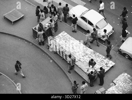 Le vivaci strade di Nairobi si animano con un ritmo unico. Questa sorprendente immagine in bianco e nero cattura un momento della vita quotidiana nella capitale keniota, dove una grande pila di mattoni viene manovrata con cura attraverso un intersezione trafficata. I residenti locali e i passanti si riuniscono intorno, contribuendo alla vivace energia della città. La scena mette in risalto lo spirito industrioso di Nairobi e la stretta comunità che definisce il suo paesaggio urbano. Foto Stock