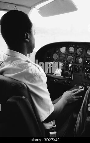 Sopra il Serengeti: Un pilota vedrà i vasti paesaggi della Tanzania. Questa sorprendente fotografia in bianco e nero cattura la prospettiva di un pilota che sorvola la vasta distesa della Tanzania. Il complesso quadro strumenti dell'aereo domina il telaio, suggerendo le sfide e i premi della navigazione in questa iconica nazione africana. L'immagine evoca un senso di avventura e sottolinea la bellezza remota della Tanzania, offrendo un punto di vista unico sul terreno diversificato del paese. Foto Stock