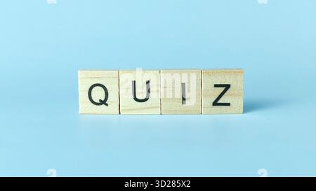 Piastrelle di Scrabble in legno che scrivono il "QUIZ" di Word su sfondo azzurro per l'istruzione, i test e la valutazione delle conoscenze Foto Stock