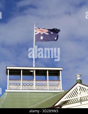 Bandiera australiana che sventola su un palo in cima a un edificio con un cielo parzialmente nuvoloso sullo sfondo Foto Stock