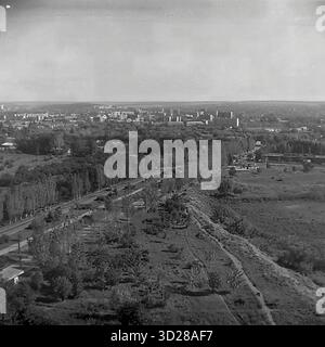 Archivio foto in bianco e nero scattata a Sloviansk, Ucraina, nell'agosto 1997. Si tratta di una vista panoramica ad alto angolo della citta', presa dalla SKTB (Special Design and Technological Bureau). Lo scatto cattura un vasto paesaggio urbano, mostrando i quartieri residenziali della città all'orizzonte, compresi gli edifici a più piani. In primo piano, è visibile una grande zona verde, possibilmente un parco o una cintura forestale, con una strada principale che corre accanto ad essa. Questa immagine documenta l'aspetto della città alla fine degli anni '1990 Foto Stock