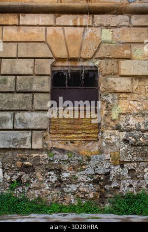 Una finestra in un muro di conci del XVII-XVIII secolo in foro Italico a Palermo, Sicilia, Italia. La parte inferiore del muro è invece costruita in muratura di macerie Foto Stock