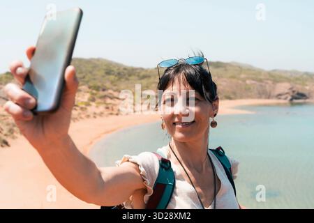 Donna che scatta un selfie durante un'escursione costiera con vista sulla spiaggia Foto Stock