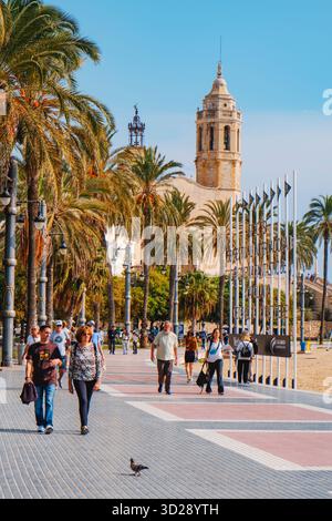 Sitges, Spagna - 17 ottobre 2025: Persone che camminano lungo il Passeig de la Ribera a Sitges, Spagna, vicino alla spiaggia e all'insegna del 58° Secolo Foto Stock