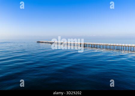 Lungo molo di legno che si estende nelle acque blu e calme del lago Issyk-Kul sotto un cielo sereno, vista aerea, Kirghizistan Foto Stock