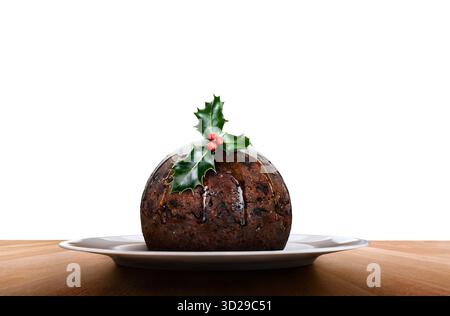 Un tradizionale budino natalizio su un piatto rotondo con un rametto di agrifoglio e frutti di bosco in cima a un tavolo di legno isolato su uno sfondo bianco. Foto Stock