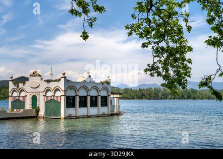 Storica pensione bianca sulle rive del lago Banyoles, Catalogna, Spagna, con acque calme e montagne sullo sfondo Foto Stock