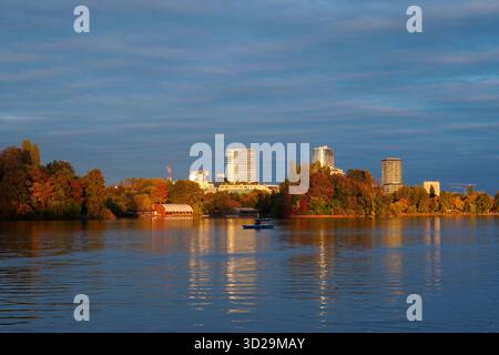 Splendido paesaggio autunnale all'ora d'oro nel parco Herastrau di Bucarest con barche sul lago, alberi colorati e torri di uffici in lontananza Foto Stock