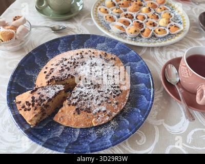 Torta con scaglie di cioccolato su un piatto in ceramica a motivi geometrici. Vacanze e stile di vita. Cibo in tavola ricoperto di tovaglia. Foto Stock