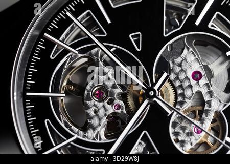 Primo piano dettagliato di un orologio scheletrico, che rivela ingranaggi, ingranaggi e gioielli viola. Questa immagine ad alto contrasto mette in risalto la maestria artigianale e il motore di precisione Foto Stock