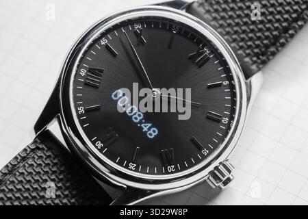 Elegante orologio da polso tonalità argento con quadrante nero spazzolato, numeri romani e una lettura digitale dell'ora. Perfetto per un abbigliamento formale, per affari Foto Stock