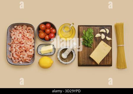 I gamberetti, i pomodori ciliegini, l'aglio e il prezzemolo si trovano ordinatamente su un tavolo insieme a limone, burro, olio d'oliva, formaggio e pasta Foto Stock