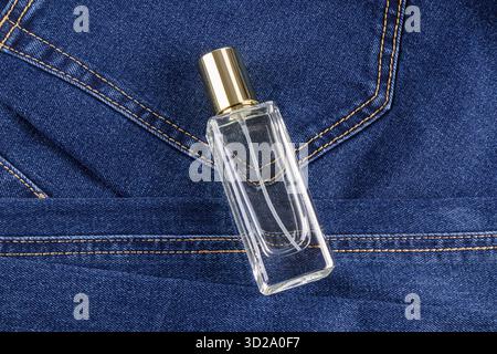 Un'elegante bottiglia trasparente di profumo da uomo si trova sui jeans blu. vista dall'alto. vista ravvicinata. macro. Un modello di bottiglia vuota. Presentazione delle fragranze Foto Stock