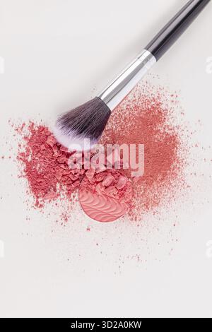 Una bella spazzola per il trucco è adagiata su un campione di rossore sparso secco in un tono rosa su sfondo bianco. Vista verticale superiore. cosmetici decorativi Foto Stock