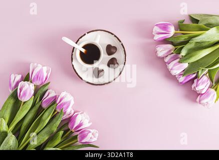 Tulipani al lilla primaverile e una tazza di caffè aromatico su un piattino con cioccolatini a forma di cuore. sfondo festivo. una copia dello spazio Foto Stock