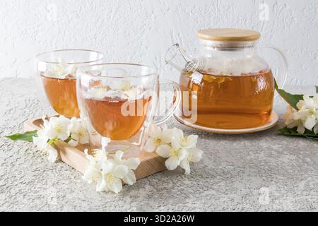 Vista frontale tazza in vetro a doppio fondo con fragrante tè di gelsomino, fiori di gelsomino e teiera in vetro con tè appena fatto. Cerimonia del tè Foto Stock