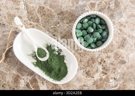 Tavolette di polvere e spirulina in ciotole su un tavolo di marmo. vista dall'alto. superfood, integratore alimentare. fonte di proteine vitaminiche e beta-carotene Foto Stock