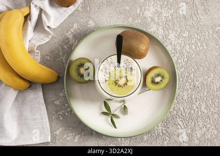 Vista dall'alto di un bicchiere di frullato di kiwi e banana con semi di chia. dessert delizioso e salutare. fonte di fibre alimentari. sfondo grigio in cemento Foto Stock