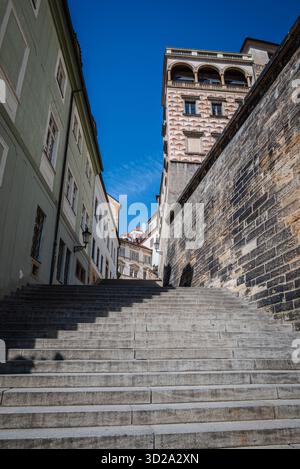 Scale che si snodano tra gli edifici su una collina a Praga, Repubblica Ceca, che conducono verso il Castello di Praga, fotografate contro un cielo azzurro. Foto Stock