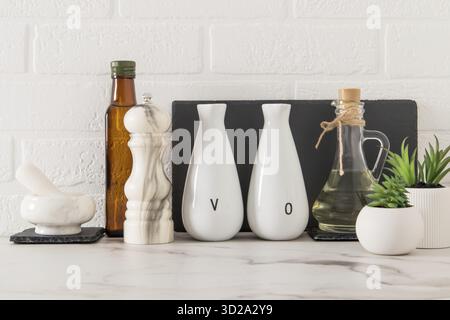 Elegante sfondo bianco della cucina con utensili da cucina e piante di casa in vaso verde su un piano di marmo bianco Foto Stock